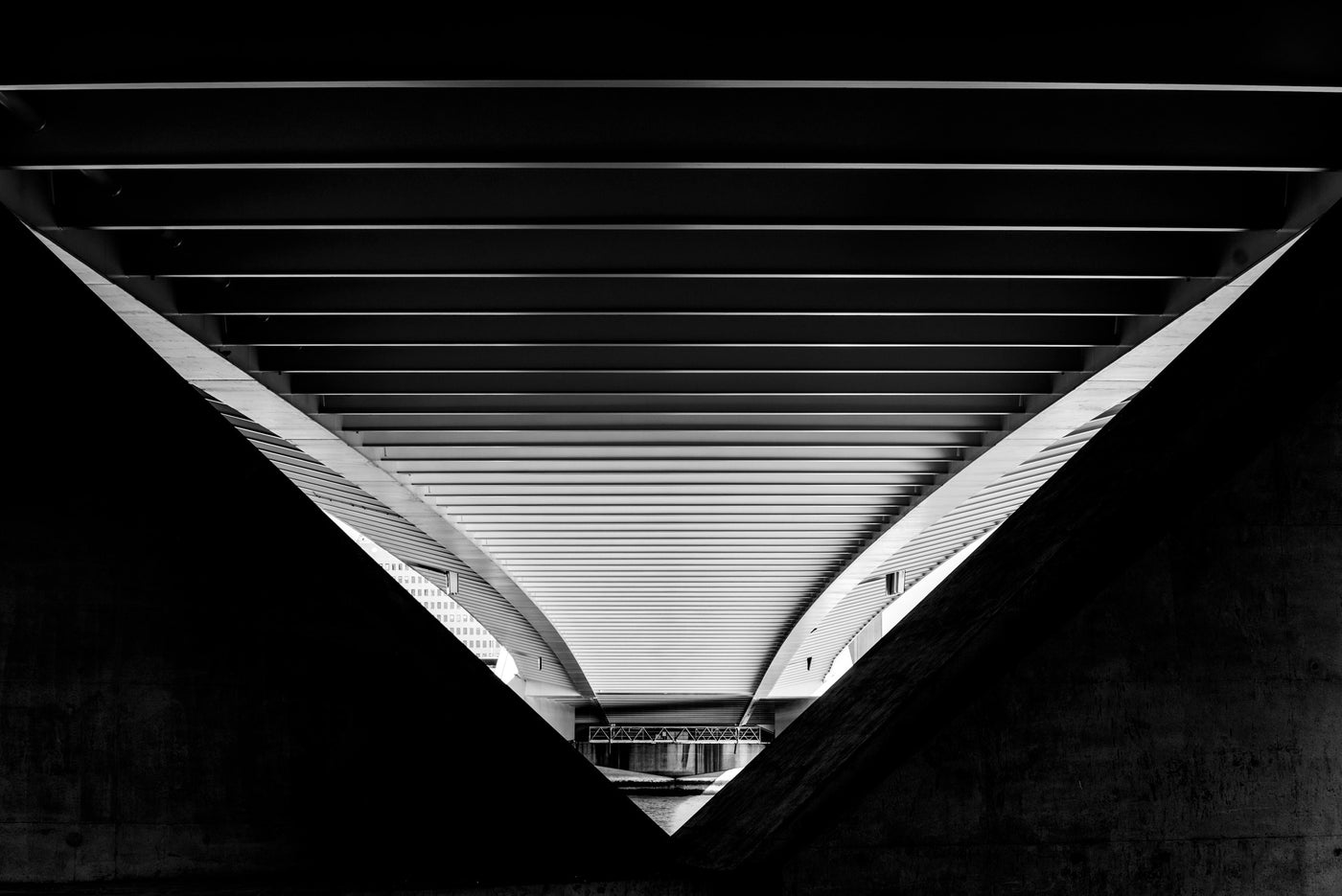 Black and white architectural photograph of a modern triangular concrete structure, viewed from below looking up through the slatted ceiling and curved concrete sides of the Erasmusbrug in Rotterdam.