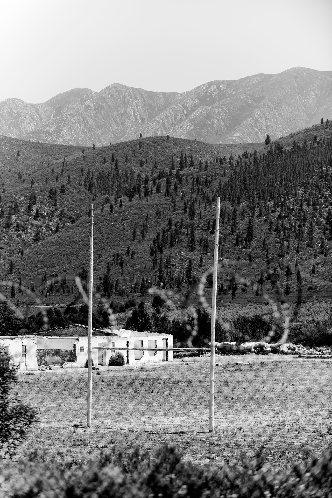Black and white landscape with mountains and a field, featuring barbed wire.