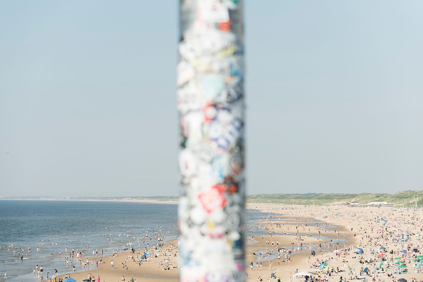 Stickers on a pole at Scheveningen Pier, with the busy summer beach in the background.