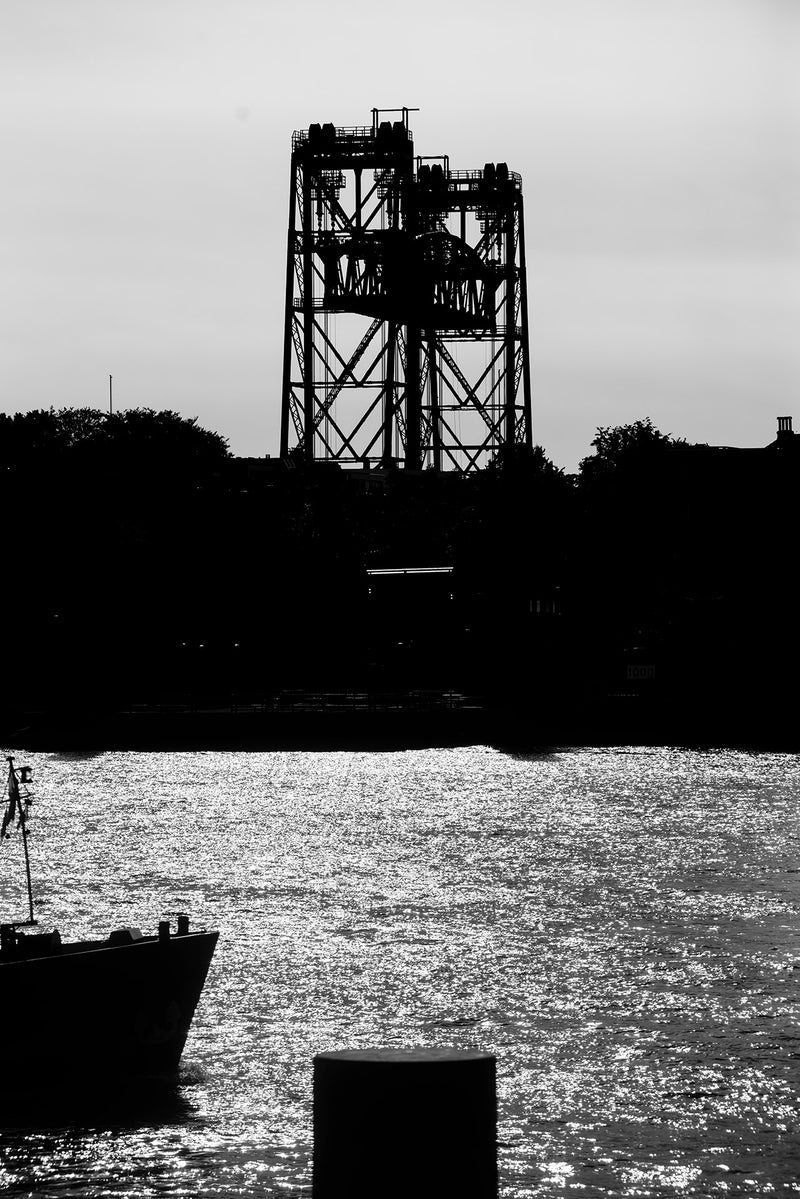 Black and white image of the Nieuwe Maas river and industrial structures beyond.