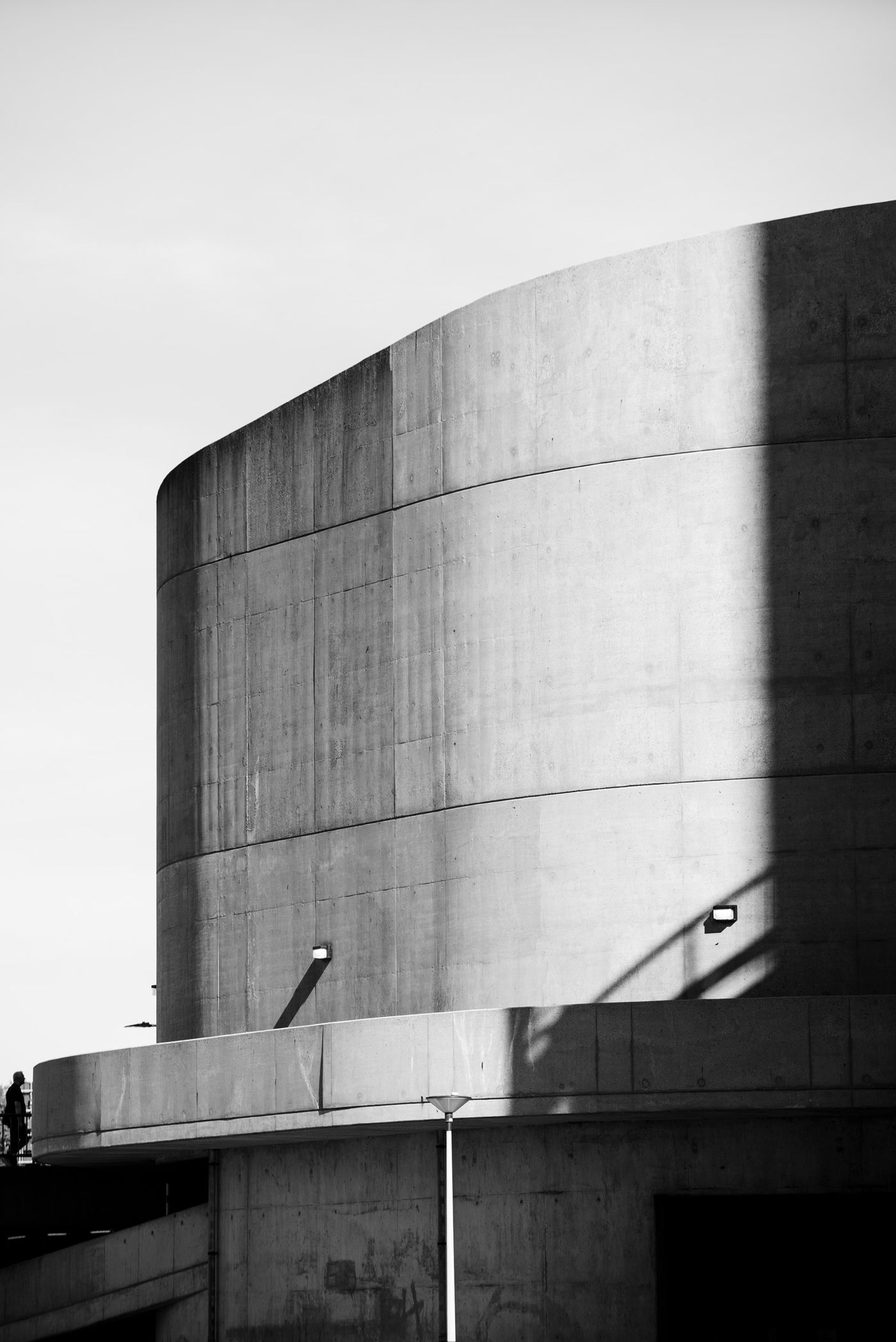 Black and white architectural photograph of a modern curved concrete structure with strong shadows and geometric lines.