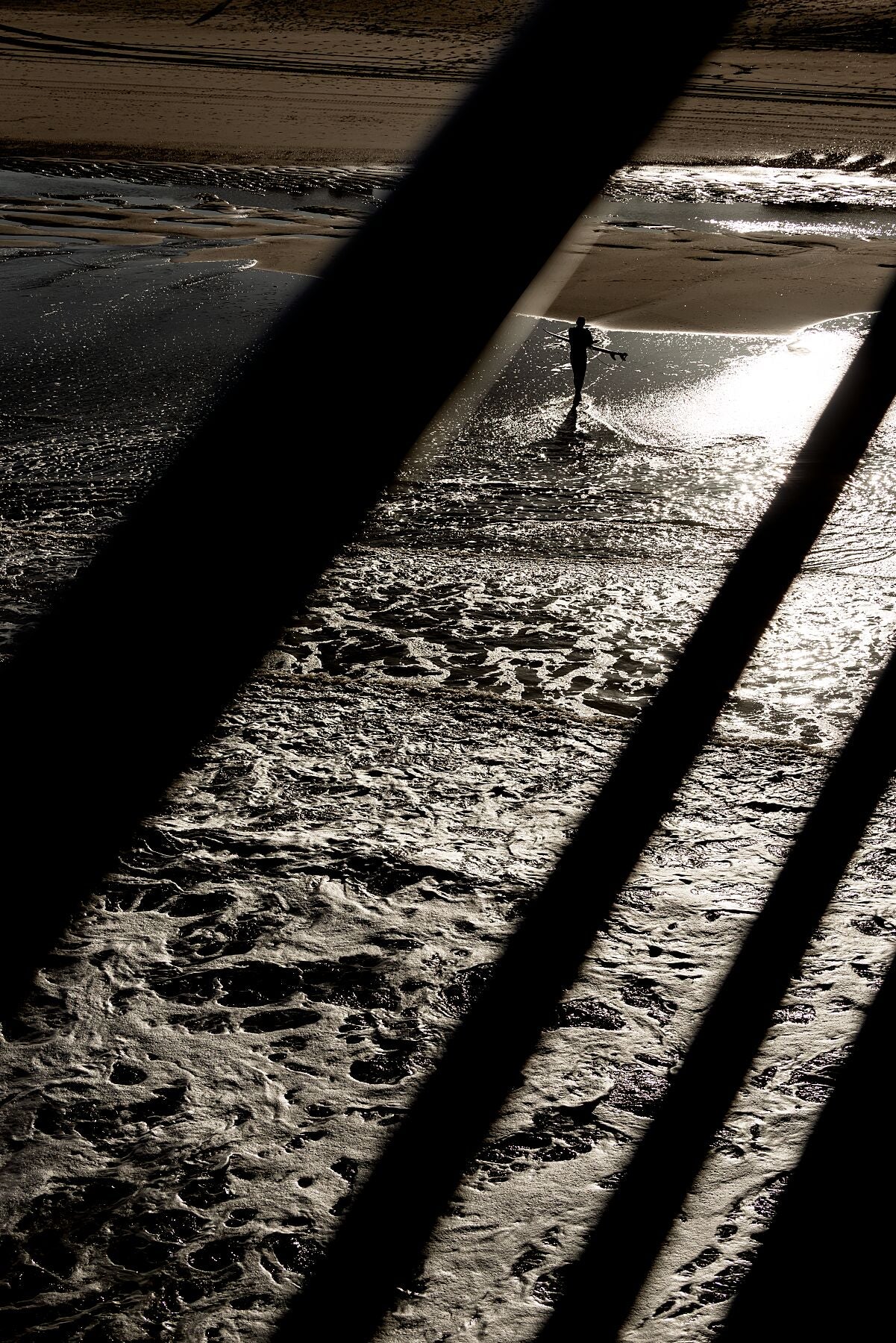A surfer and the sea. The railing of the Scheveningen Pier bisect the scene.