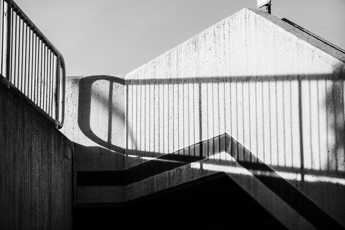 Black and white architectural photograph of concrete stairs and walls with strong shadow patterns cast across the surfaces.