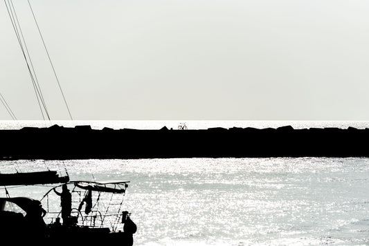 A yacht silhouetted with a bicycle in the background passes through the harbour area at Scheveningen