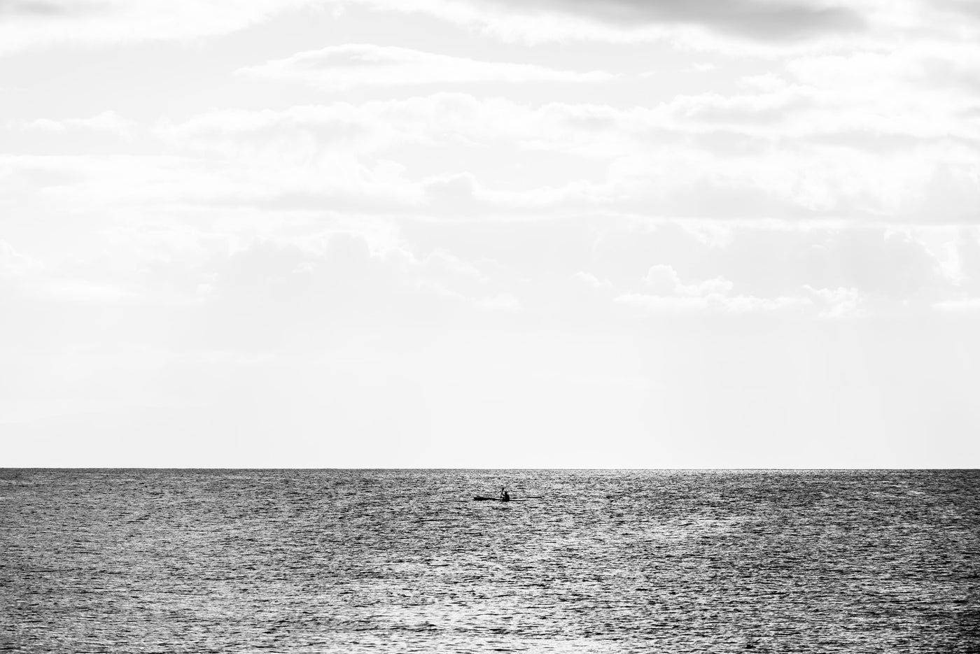Black and white seascape photograph showing a calm ocean horizon in cape Town under a cloudy sky, with a canoe.
