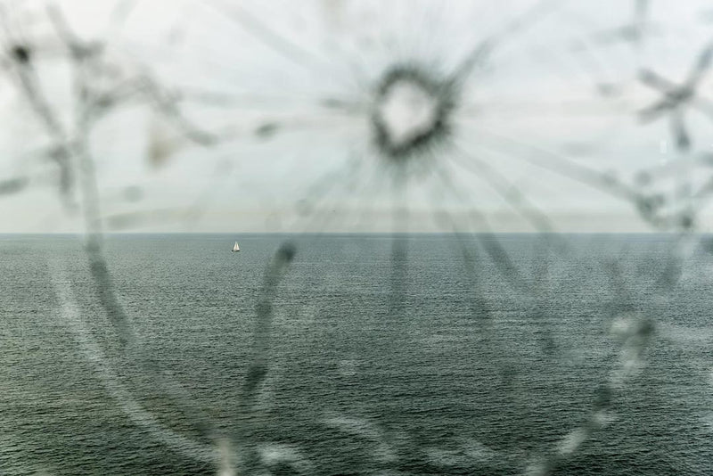 An editorial style photograph of a broken window and the sea beyond.