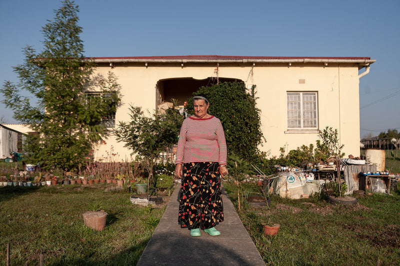 A portrait of a lady in front of her small house.