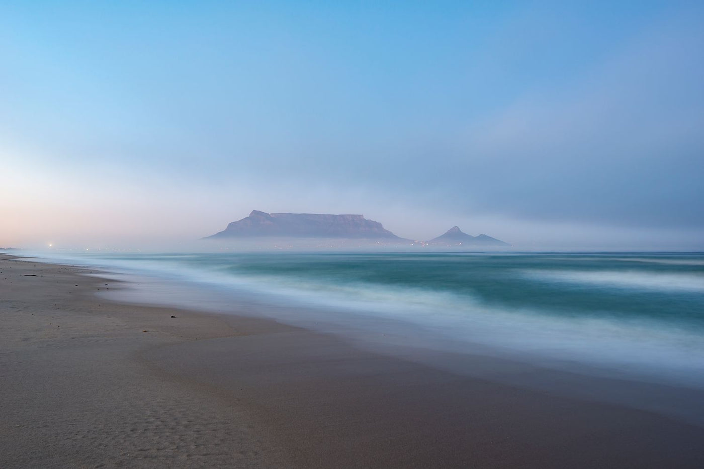 A slow shutter speed captures movement in the waves on the coastline with Table Mountain in the background.